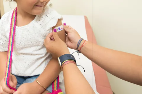 little girl looking down as a band aid gets put on her arm