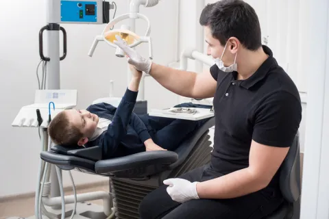 male dentist high fiving boy laying down in dental exam chair