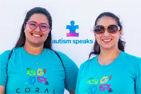 2 woman wearing glasses with the autism speaks logo behind them