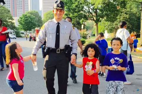 Photo of a first responder holding hands with children at a safety fair