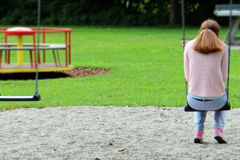 Girl sitting on a swing set alone in a park 