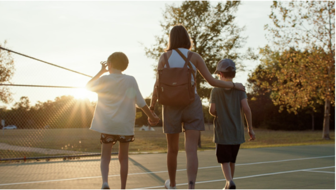 A women  holding hands with two boys on a tennis court at sunset with their backs to the camera