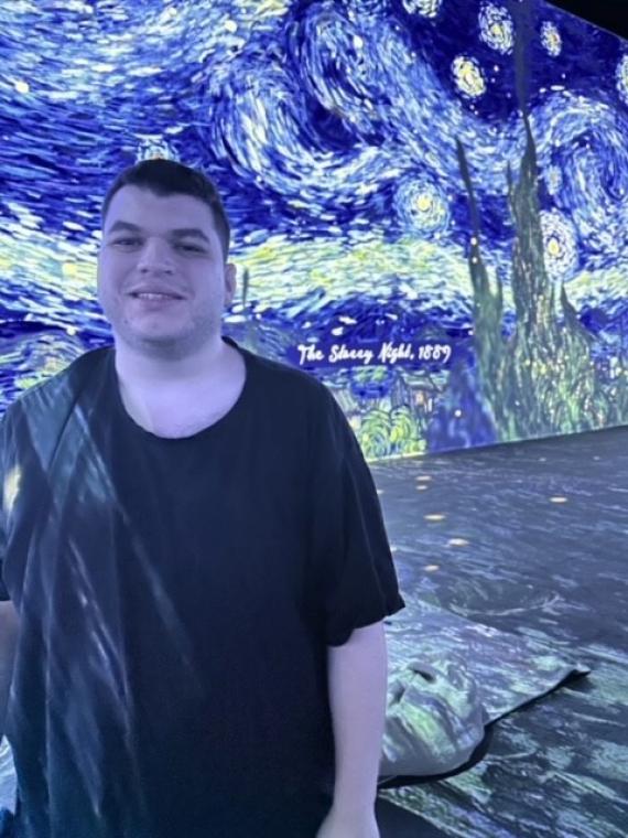 A young man in a black shirt stands in front of a projected Starry Night image