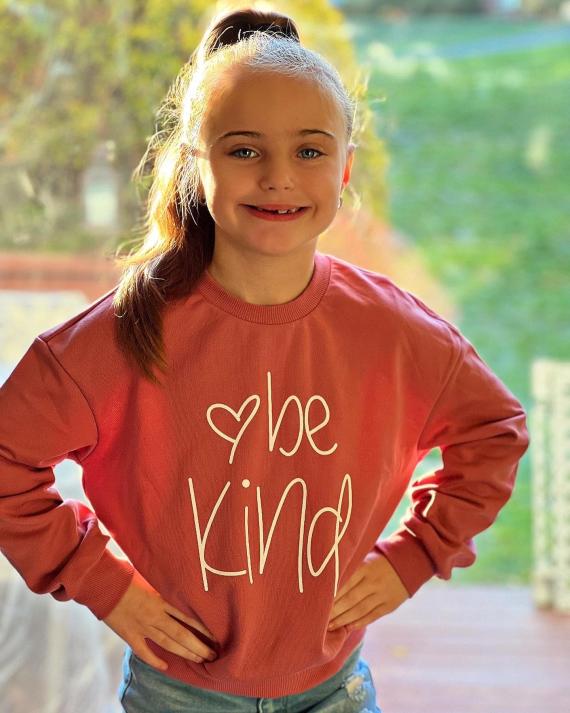 Scarlett smiling with her hands on her sides wearing a 'Be Kind' sweater