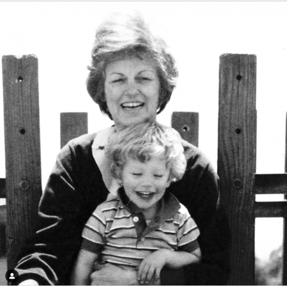 A black and white photo of a mother and her toodler son. In front of a wooden fence, both laughing 