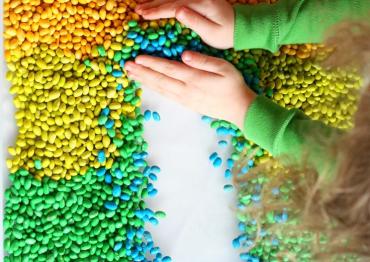 Sensory game with different colored beans on a table and a toddler touching them