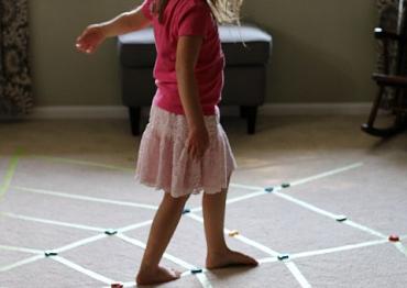 little girl in a pink shirt and skirt walking on a diy sensory spider web on the floor