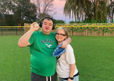 man in green eagles shirt and headphones posing with smiling man in black shirt on a ball field