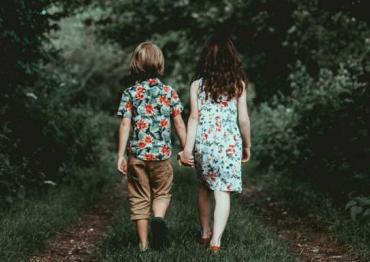 two children walking on a wooded path while holding hands