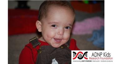 A baby in overalls with the ADNP Kids Research Foundation logo