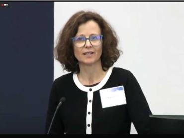 Chiara Servili in black cardigan standing at podium microphone
