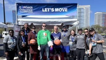 Group of people posing outdoors under a “Let’s Move” banner at an Autism Speaks Empower Challenge event