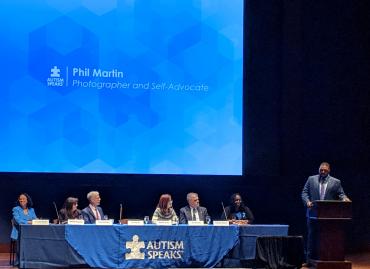 Phil Martin presenting at podium with panelists sitting at long table