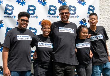 Black family of five standing in front of Black Autism Support Society step-and-repeat