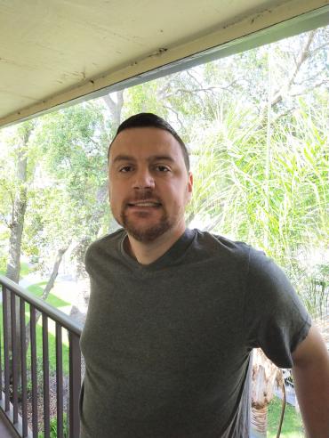 Ian H. wearing a grey shirt standing on a balcony