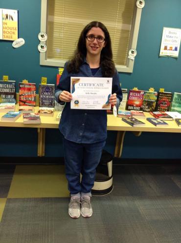 Kelly volunteering at the library, holding up a certificate