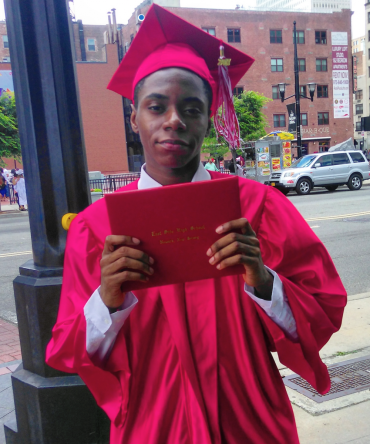 Khali Raymond wearing a graduation cap and gown, holding a diploma