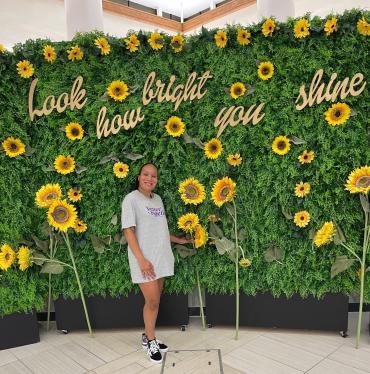 Saida standing in front of wall of sunflowers and words "look how bright you shine"