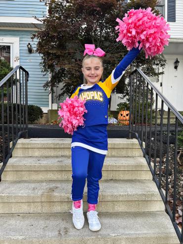 Scarlett in her cheerleading uniform holding up a pink pom-pom