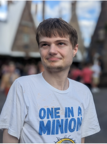 A young white man looks off in the distance, he wearing a white t-shirt that says "one in a minion" in blue font 