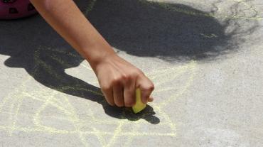 a child drawing on pavement with yellow chalk