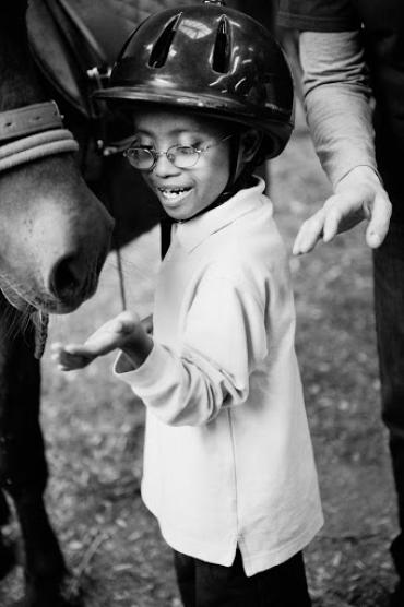 a child with glasses petting a horse at GallopNYC