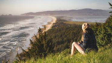 a woman sitting on a grassy hill over looking the ocean