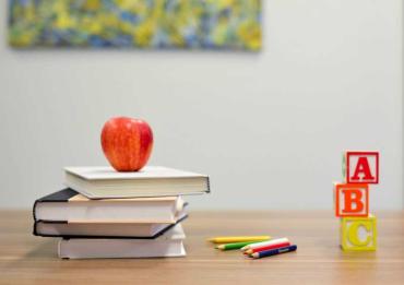 a stack of books, an apple on top, blocks and colored pencils on a desk