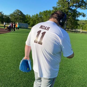 back view of man wearing white jersey with noah 11 on it walking on green turf holding a blue glove