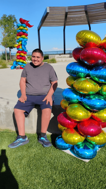 boy sitting next to a pillar of balloons