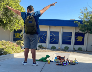 boy with a backpack and his arms in the air outside of school