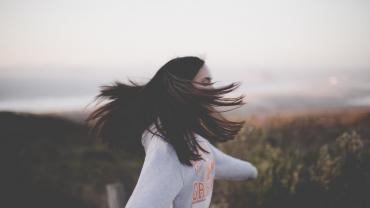 a brunette woman in a white shirt spinning around in a field