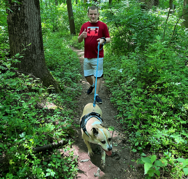 man in a red shirt walking a dog through the forest