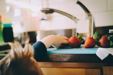 toddler reaching to grab a strawberry off the kitchen counter