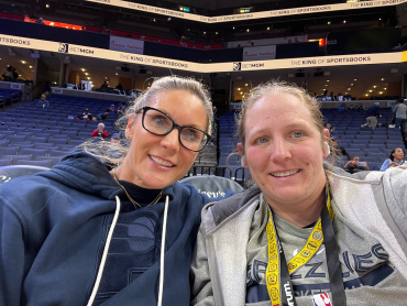 two women smiling for a selfie in a basketball arena