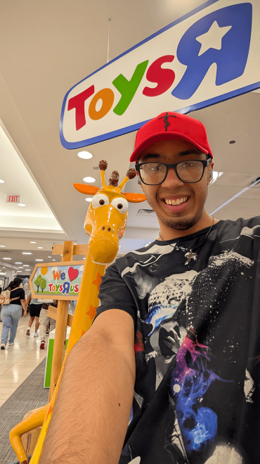 young man in a red hat standing in front of the Toys R Us giraffe