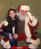 A little girl sitting on Santa's lap during a Caring Santa event in 2017