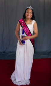 Saida M wearing white dress, pink pageant sash and crown while holding award