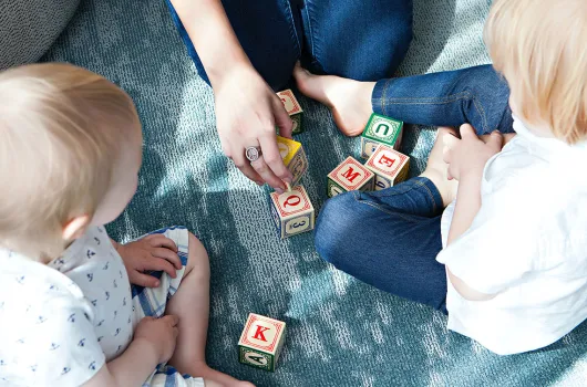 An adult and two children playing with lettered blocks on the floor